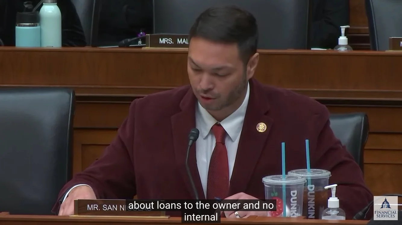 Rep. San Nicolas, sitting in Congress and speaking, with two plastic Dunkin iced coffee cups next to him